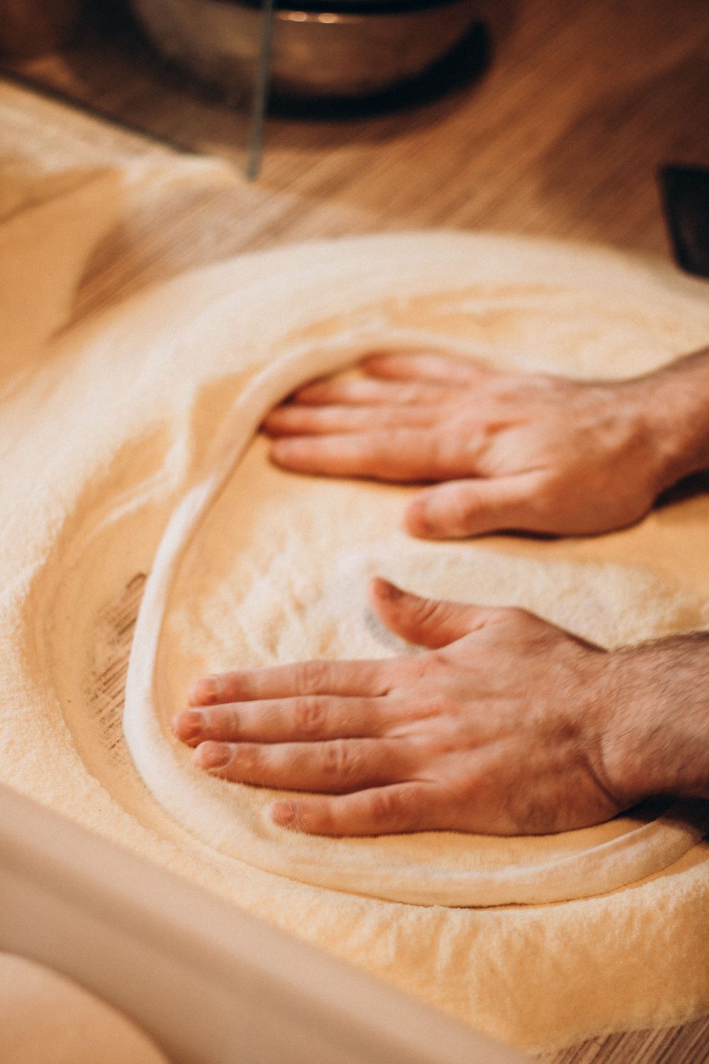 Hands stretching pizza dough on a floured wooden counter